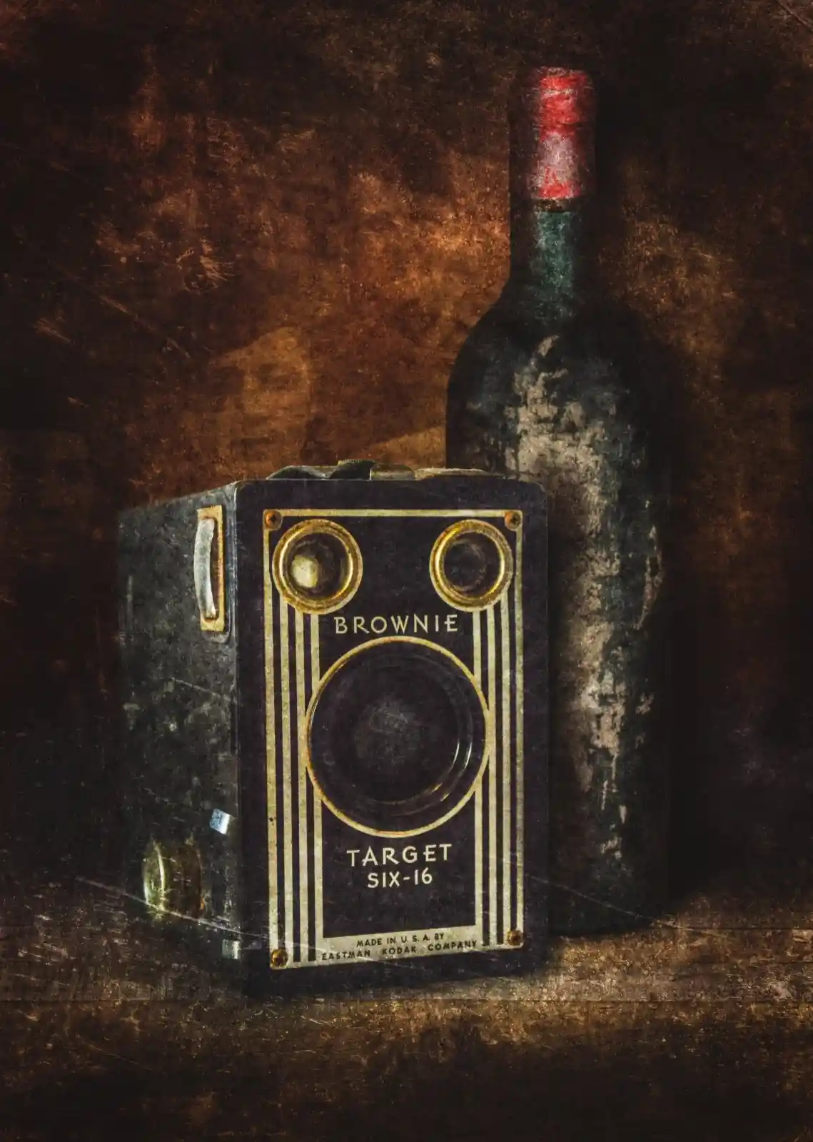 An old Brownie camera sits on a worn, dusty shelf, beside a weathered bottle of wine. The camera’s black metal is scratched and aged, its golden detailing still glimmering with stories untold. The bottle, a silent companion, seems to hold the remnants of forgotten nights. This pairing speaks of moments captured and those lost to time—a nostalgic dance between memory and oblivion, between light and shadow.