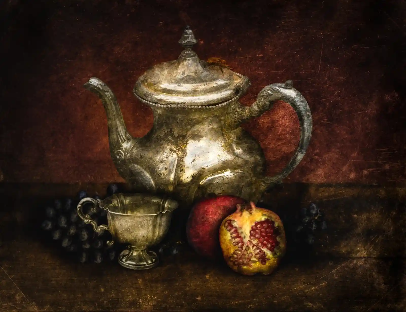 An antique silver teapot and cup are set alongside a halved pomegranate and a cluster of grapes. The rich, shadowed background accentuates the tarnished elegance of the silver, casting an atmosphere of forgotten grandeur and whispered secrets of what came before.